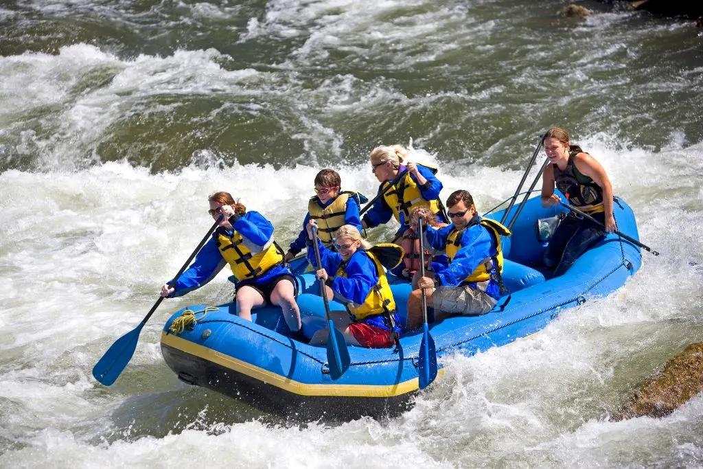 Group of six people in a blue boat rafting along the river in upstate New York. 