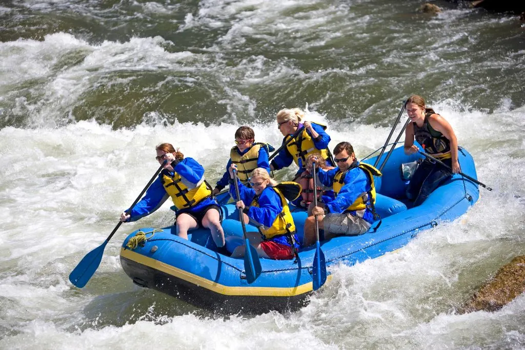 Group of six people in a blue boat rafting along the river in upstate New York.