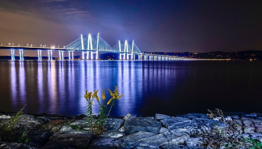 View of the Cuomo Bridge all lit up in the evening from the waterfront area at night in Tarrytown.