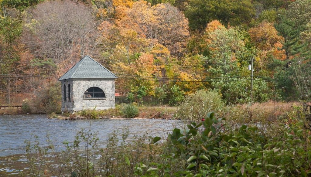 View of a stone pavillion sitting by a lake with fall foliage in the background at Tarrytown Lakes Park.