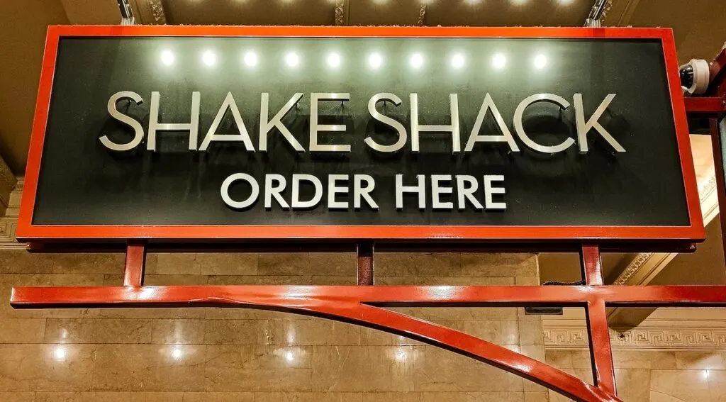 Enormous Shake Shack sign where you order food at one of the fun restaurants in NYC for kids. The letters are white and the sign is black with wooden trim, 