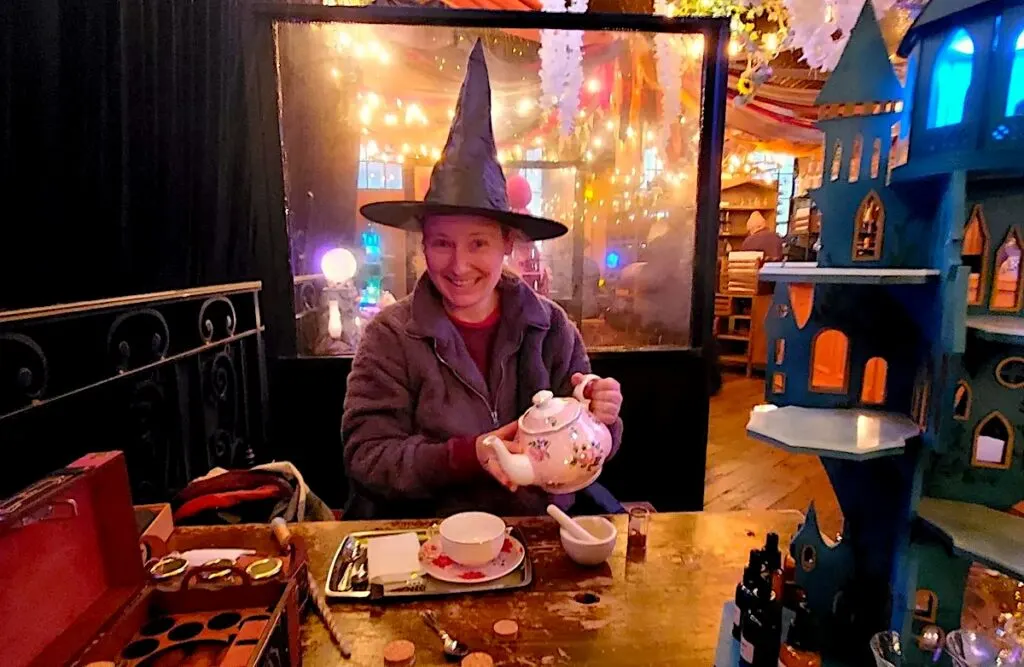 Me holding a white tea pot with a black witch hat on as I sit and enjoy afternoon tea at the cauldron in NYC. 