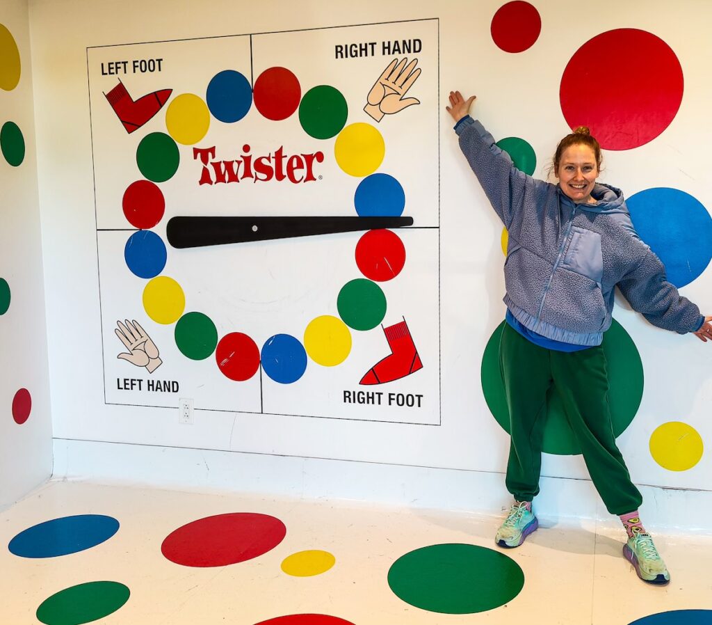 Me standing in front of a giant Twister board on a blue fleece and green pants.