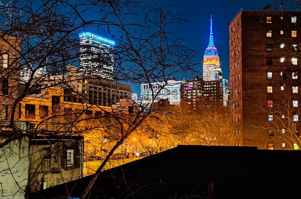 View of the Empir State Building all lit up at night on the Highline. 