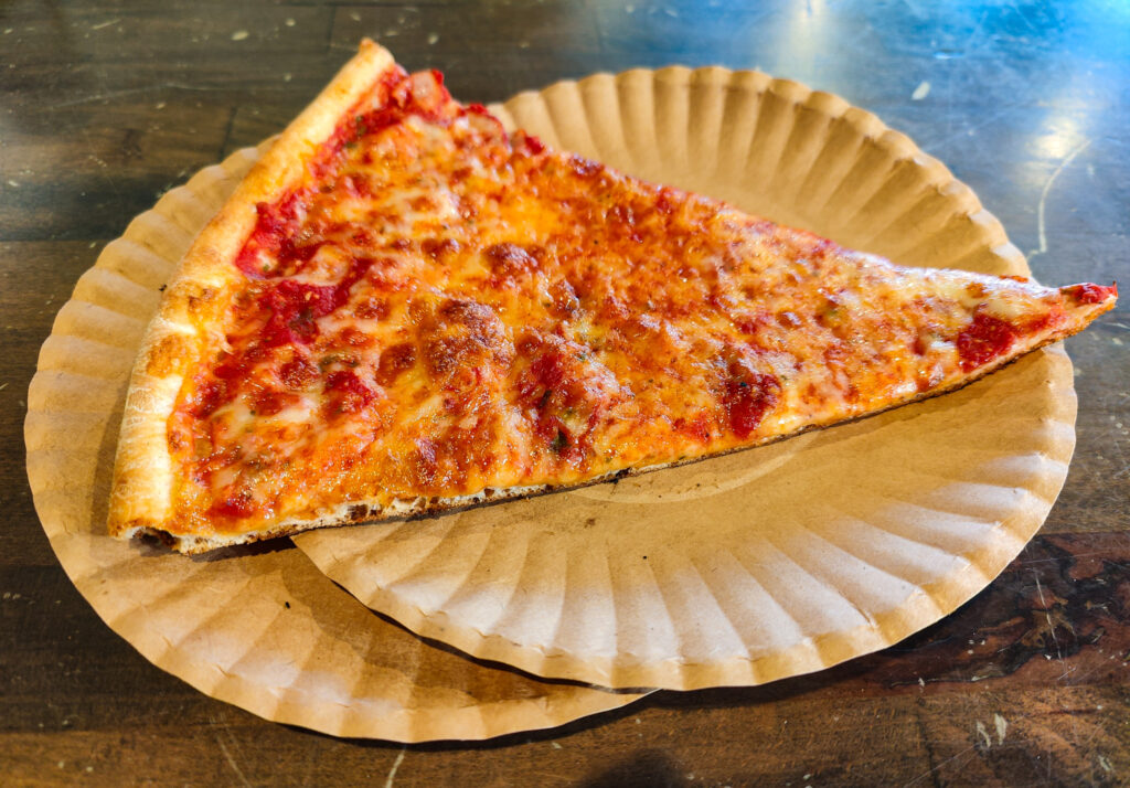 Aerial view of a traditional slice of NYC-style pizza on two white plates that sit on a green table. This is the best pizza in NYC. 