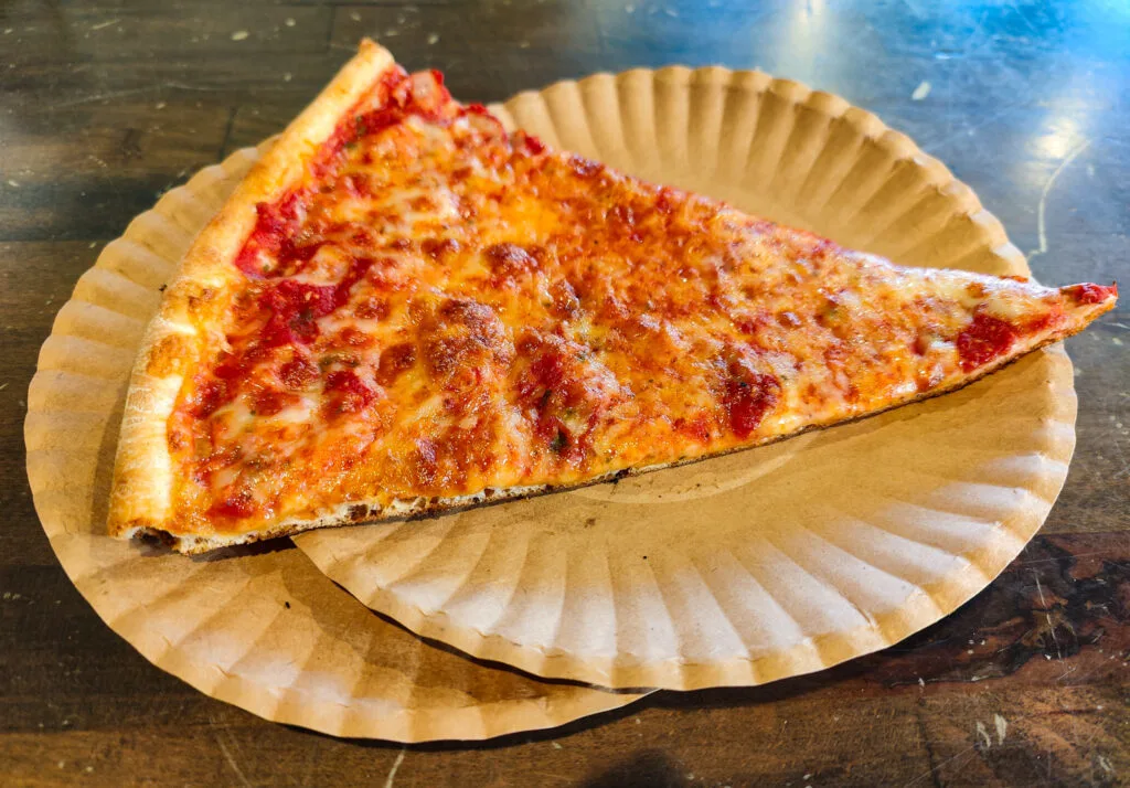 Aerial view of a traditional slice of NYC-style pizza on two white plates that sit on a green table. This is the best pizza in NYC. 