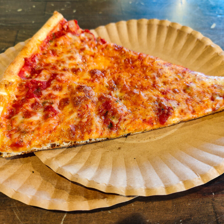 Aerial view of a traditional slice of NYC-style pizza on two white plates that sit on a green table. This is the best pizza in NYC.