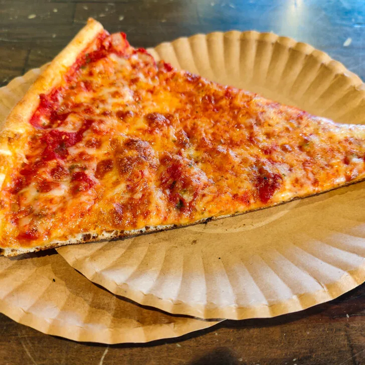 Aerial view of a traditional slice of NYC-style pizza on two white plates that sit on a green table. This is the best pizza in NYC.